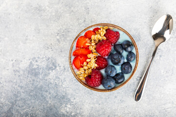 Bowl of granola with yogurt and fresh berries on a texture table. Yogurt berries, acai bowl, spirulina bowl. Healthy food, balanced breakfast. Strawberries, blueberries, kiwi, peach, almonds and chia.