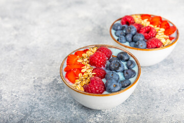 Bowl of granola with yogurt and fresh berries on a texture table. Yogurt berries, acai bowl, spirulina bowl. Healthy food, balanced breakfast. Strawberries, blueberries, kiwi, peach, almonds and chia.