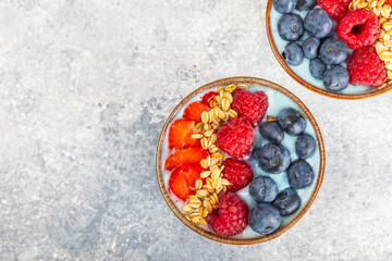 Bowl of granola with yogurt and fresh berries on a texture table. Yogurt berries, acai bowl, spirulina bowl. Healthy food, balanced breakfast. Strawberries, blueberries, kiwi, peach, almonds and chia.