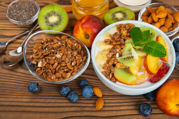 Bowl of granola with yogurt and fresh berries on a texture table. Yogurt berries, acai bowl, spirulina bowl. Healthy food, balanced breakfast. Strawberries, blueberries, kiwi, peach, almonds and chia.