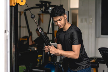 Fototapeta na wymiar A young handsome asian man does a set of tricep rope pushdowns on the cable machine at the gym.