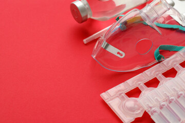 Fototapeta na wymiar Coronavirus treatment concept. A medical face mask nebulizer for treatment of respiratory tract and packs of ampoules flat layed on red background