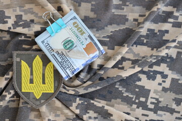 Ukrainian army symbol and bunch of dollar bills on military uniform. Payments to soldiers of the Ukrainian army from United States, salaries to the military. War support