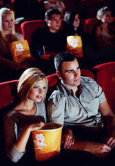 Cinema, love and couple with popcorn, watching film or eating on romantic date together. Movie night, man and woman in theater with snacks, romance and sitting in auditorium to relax at show premier.