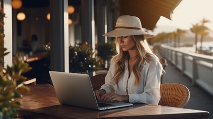Beautiful woman works at a laptop at a coastal cafe. Concept of successful young independent woman. AI - obrazy, fototapety, plakaty