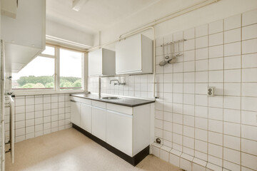 a kitchen with white tiles on the walls and counter space in front of the sink, window to the left