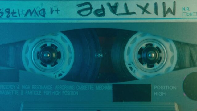 Audio cassette with handwritten mixtape sign playing in a retro tape recorder under colorful neon light. Extreme close-up view, no people