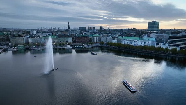 Aerial shot of Alster lake with fountain, framed by the striking TV tower and Hamburg skyline, with Alster tourist ship gliding along the serene waters. Hamburg's Alster lake with iconic skyline.
