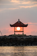 Great sun ball in a small temple in Bali, on the sandy beach of Sanur. Sun ball on the horizon and clouds in the sky. Everything in the morning over the sea of ​​Indonesia
