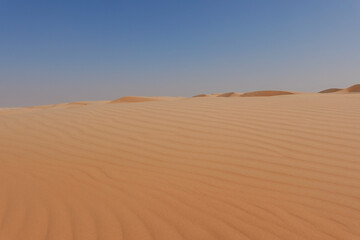 Fototapeta na wymiar Shot from below golden desert sand and small dunes on the horizon and blue sky.
