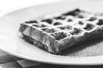 Black and white portrait of a belgian tasty delicious waffle with powder sugar as a topping on it,...