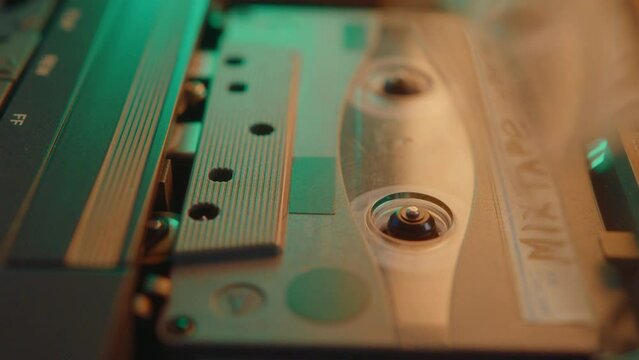 Male hand inserting audio cassette into retro tape recorder and playing the music in room with warm light. Extreme close-up view, zoom-out shot