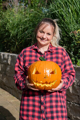 Blonde woman in the garden presents a self-carved pumpkin with face as decoration for Halloween time