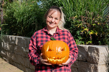 Blonde woman in the garden presents a self-carved pumpkin with face as decoration for Halloween time