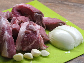 large pieces of pork on a green plastic chopping board with coarsely chopped onions and garlic...