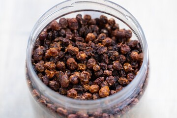 A close up portrait of a plastic pot or jar full of fresh dried loose buckthorn tea in it. The herb is ready to be used in a relaxing cup of the warm beverage or drink for some zen time.