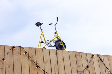 A close up portrait of an old vintage home trainer or bike standing on top of a building with wooden planks as the front. This could be the top of a gym or sport store.