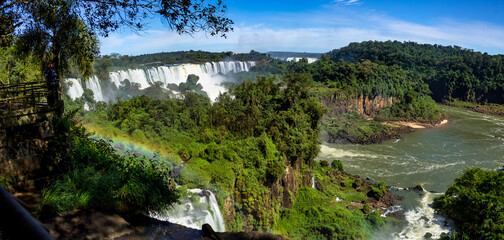 Panorama of Iguazu (Iguacu) waterfall with rainbow cascade waterfalls landscape in Argentina. Powerful natural falls in greenery rainforest, summer sun day. World nature concept. Copy ad text space