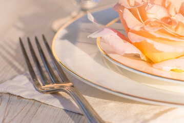 Romantic table setting; close up for salmon rose flower on the white plates, fork on the white napkin son sunlight