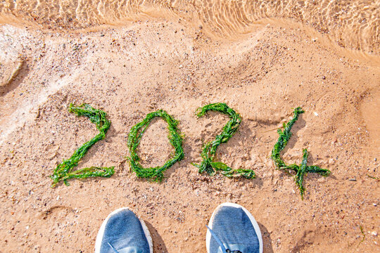 2024 Happy new year  image with the numbers 2024 in seaweed on a sandy beach. A pair of blue shoes give perspective. Eco picture with good copy space.
