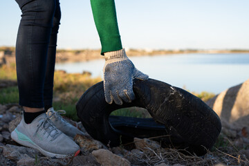 Unrecognizable person wearing gloves picking up a worn vehicle cover from a landfill in a coastal marine estuarine wetland. Photo with space for text.