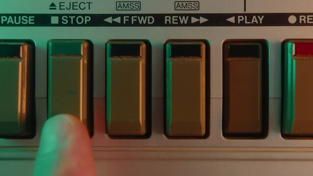 Close-up view of finger pushing Stop, Rew and Play button on retro tape recorder while playing music