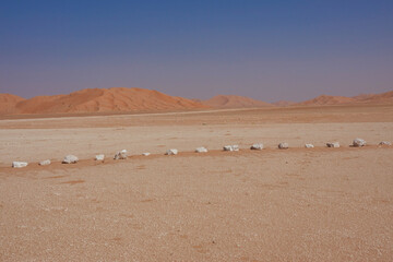 White limestone boulders in a line in the background high red dunes and blue sky.