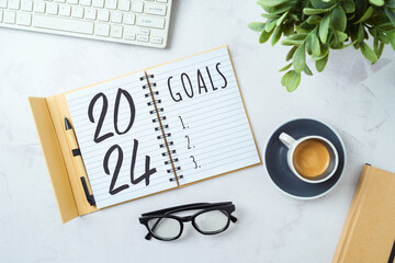 New Year 2024 goals and resolution business concept with notebook, coffee cup, computer keyboard and plant on modern office desk. Top view, flat lay