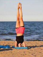Fototapeta na wymiar athletic girl performs challenging gymnastic exercises on the beach by the sea with shorts
