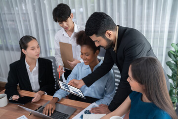 Multiracial analyst team use BI dashboard data to analyze financial report on meeting table. Group of diverse business people utilize data analysis by FIntech for success business marketing. Concord