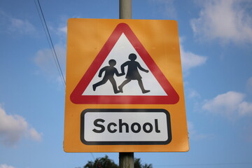 Yellow and red school sign UK blue sky in background with clouds