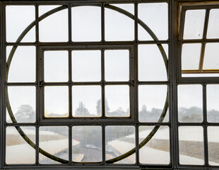 Round window, art deco design overlooking the train platform. Rain obscures the view.