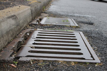 Grate of a storm sewer drain up close perspective, blurred street in background