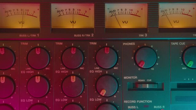Close-up shot of VU meters and knobs on analog tape recorder in studio with neon light