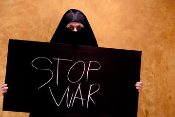 Palestinian woman in a hijab with a tired,sad look holding a banner with the inscription in chalk...