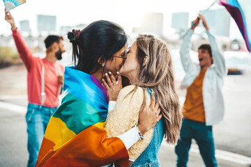 Diverse group of young people celebrating gay pride festival day - Lgbt community concept with two girls kissing outdoors - Multiracial trendy friends standing on a yellow background - obrazy, fototapety, plakaty