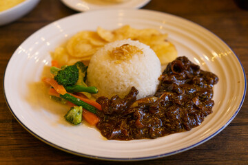Bistik, Indonesian food that identical to beef steak or beef stew served in white plate with fresh carrot and broccoli vegetables and white rice with chips
