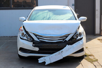 Broken white car after an accident. The headlights, hood, radiator, bumper, and fenders were...