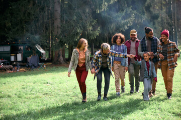 Happy multiracial families walking in nature while camping together in autumn day .