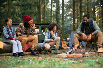 Happy black family relaxing by campfire in forest in autumn. - obrazy, fototapety, plakaty