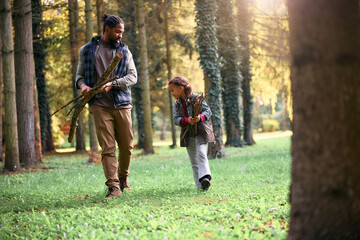 Black father and daughter collecting twigs while camping in nature.