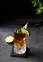 Coffee brew in a glass with tonic, ice and lime on a dark background with citrus fruit and herb. Concept craft refreshing trend drink.