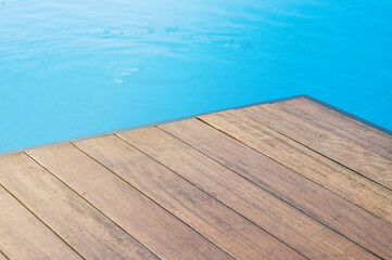 Empty wooden tabletop in front of a swimming pool with blue tiles. Concept for product presentation display with summer background.