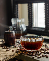 Coffee in a transparent cup, coffee beans, a transparent glass cezve and a manual coffee maker on an organic fabric on a table against the background of a window, morning, breakfast, photo in a dark k