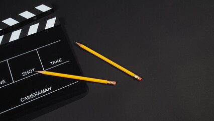 Black clapper board or movie slate with 2 pencils isolated on black background.