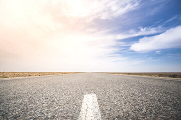 Obraz premium Car asphalt road in the middle of a hot summer steppe under the rays of the bright sun, a minimalist route in the desert