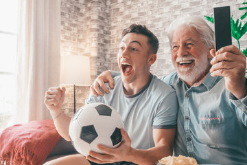 Excited couple of young boy and senior grandfather soccer fans watching a football game on tv...