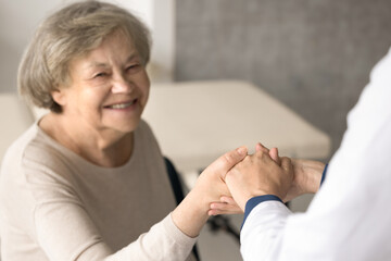 Close up smiling old woman hold doctors hand, get optimistic news after therapy. Therapist...