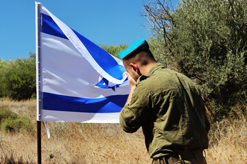 Israel Defense Forces soldier mourns in front of the Israeli national flag. Concept photo: IDF,...