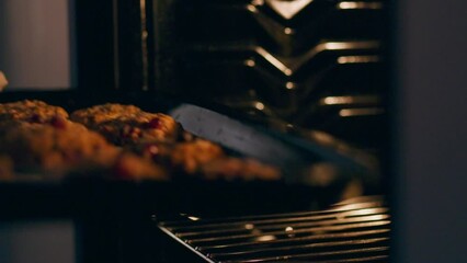 A young housewife in kitchen clothes takes ready-made cookies from the oven on a wooden table. A housewife takes out a baking tray with ready-made baked goods and uses a new recipe for making cookies.